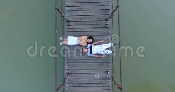 俯视图年轻夫妇的爱情金发男人和黑发女人躺在桥上的河流和向上看视频的预览图