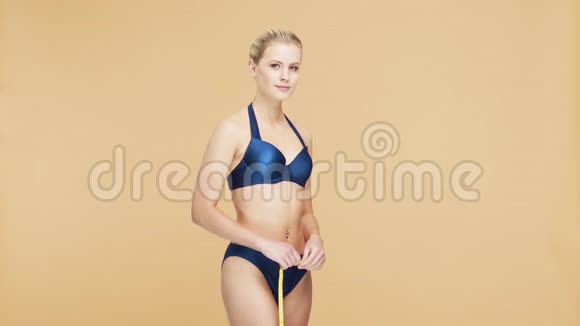 年轻美丽健康自然的金发碧眼的女人穿着蓝色泳衣测量着她完美的身材运动健身护肤视频的预览图