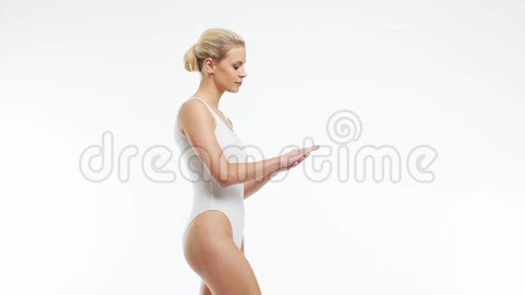 年轻美丽苗条和健康的金发女孩穿着白色泳衣涂上护肤霜按摩护肤保健视频的预览图