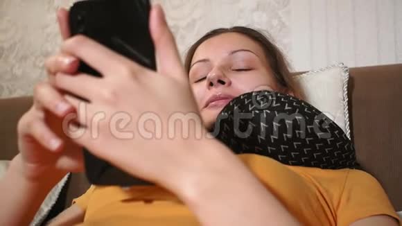 年轻漂亮的白种人女孩早上躺在舒适的卧室里用智能手机笑视频的预览图