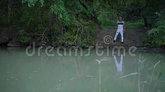 迷人的金发男子站在河的另一边水面和框架上都有苗条性感的年轻女子视频的预览图