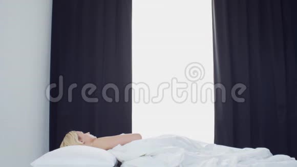 床上的年轻女子美丽的金发女孩醒来早上在卧室窗外的日光健康和休息视频的预览图