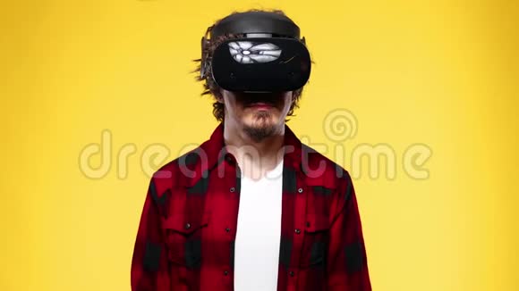 一位留着卷发的年轻人使用VR耳机在黄色背景下体验虚拟现实视频的预览图