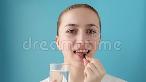 在蓝色背景下从玻璃中摄取维生素丸和饮用水的开朗女人妇女健康和保健视频的预览图