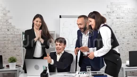 一群快乐的商人看着笔记本电脑屏幕做着庆祝胜利的手势视频的预览图