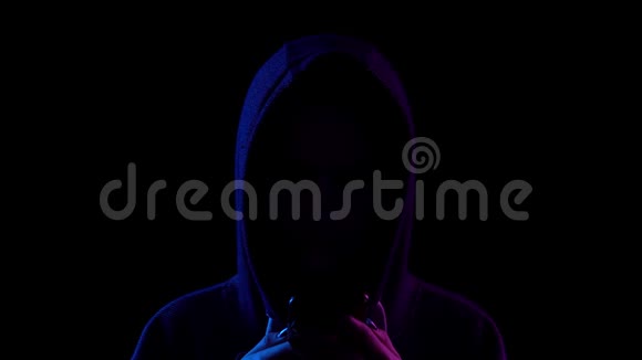 一个戴着兜帽的年轻女人手里拿着手机特写黑客通过电话攻击蓝色和红光视频的预览图