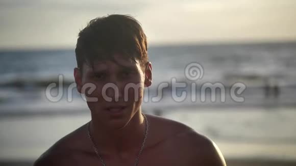 一幅英俊的年轻人的肖像这位训练有素的肌肉运动员在日落时在海滩上摆姿势视频的预览图