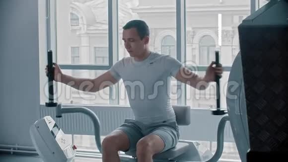 现代健身房一个男人坐在训练仪器上训练他的手视频的预览图