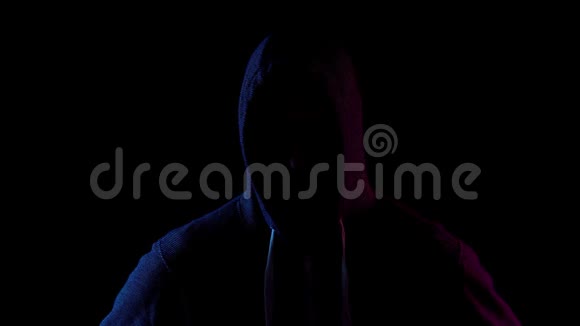一个年轻人脱下他的引擎盖攻击者站在黑暗中蓝色和红色的光落在黑色的人身上视频的预览图
