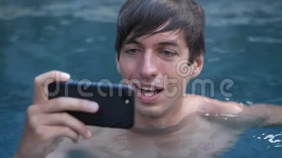 在游泳池里用智能手机观看视频的微笑年轻人特写视频的预览图