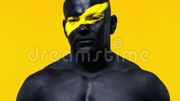 男性健美运动员脸上有黄色的艺术和黑色的身体油漆彩色肖像的家伙与健美视频的预览图