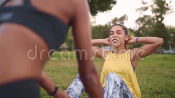 美国黑人朋友微笑着支持躺在草地上的健康年轻女子因为她在草地上做着紧缩的健身运动视频的预览图