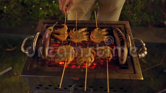 晚上的烧烤男人在烤架上做蔬菜和虾视频的预览图