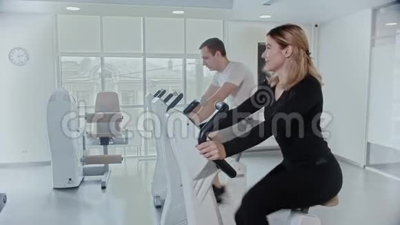 男人和女人在白色的现代健身房用运动自行车训练他们的腿视频的预览图