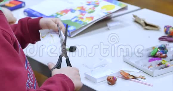 艺术工作室里的年轻艺术家或男孩坐在一张桌子旁用纸剪刀剪一个图形学习过程或视频的预览图