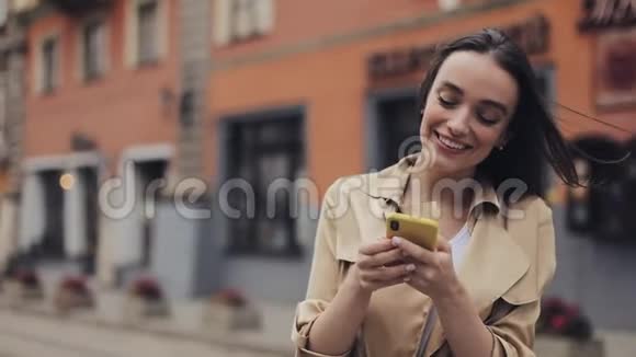 年轻迷人的微笑女人用她的智能手机站在老城街传播概念视频的预览图
