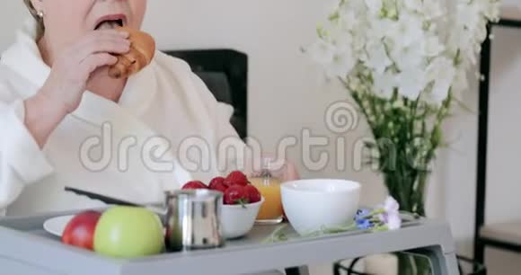 在床上吃早餐的时候把漂亮的老年妇女夹起来吃羊角面包老太太在家抢劫看电视视频的预览图