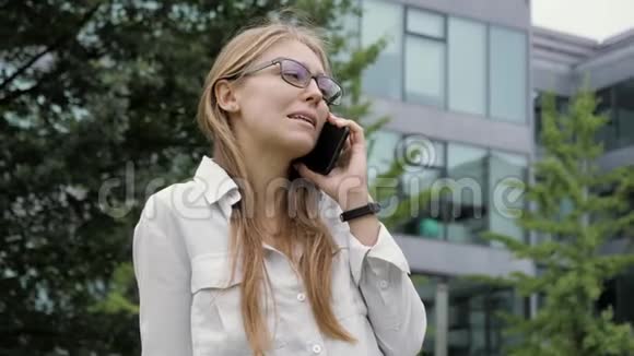 商务女性戴着眼镜金发在办公楼旁打电话视频的预览图