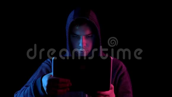 一个戴着笔记本电脑的青年黑客通过上网本进行黑客攻击蓝色和红色的光落在视频的预览图