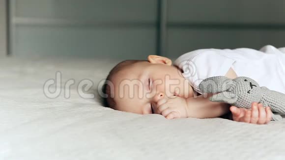 在毯子上睡着可爱的小男孩手里拿着灰色的野兔视频的预览图