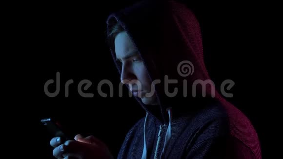 戴着兜帽的年轻人手里拿着电话黑客通过电话攻击蓝色和红色的光落在视频的预览图