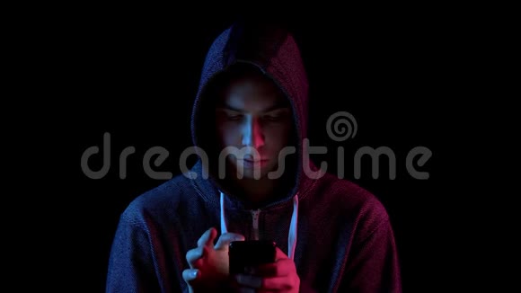 戴着兜帽的年轻人手里拿着电话黑客通过电话攻击蓝色和红色的光落在视频的预览图