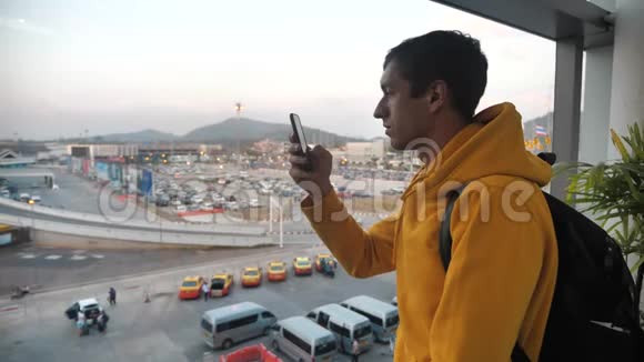 男子游客带背包的肖像站在一个大窗户前的室内使用智能手机旅行概念视频的预览图