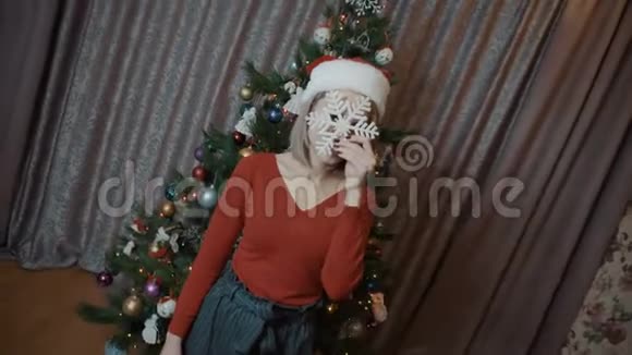 那个穿红色衣服的女孩站在圣诞树的背景上身上有一片雪花戴圣诞帽的女孩视频的预览图