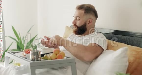 30多岁的大胡子在床上吃早餐时吃药年轻人一边喝着药片一边喝着杯水视频的预览图