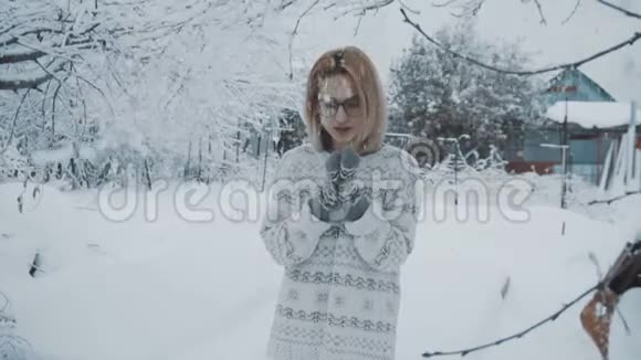 戴着眼镜穿着毛衣戴着手套的女孩站在冬天降雪下的街道上视频的预览图
