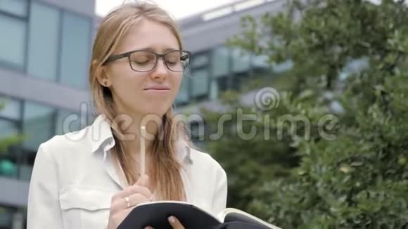 戴着眼镜的漂亮沉思的年轻学生拿着一本笔记本和一支铅笔看着远方思考着视频的预览图