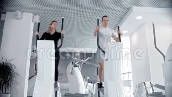 男人和女人在白色的现代健身房用运动自行车训练他们的腿视频的预览图