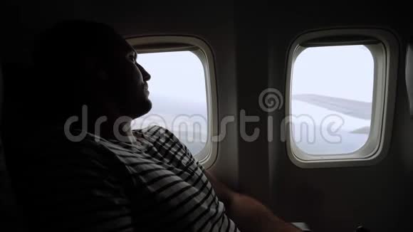 在飞行过程中英俊的年轻人透过飞机窗户看着视频的预览图