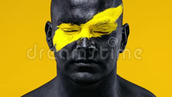 男子健美运动员的特写肖像脸上有黄色的艺术和黑色的身体油漆彩色照片视频的预览图