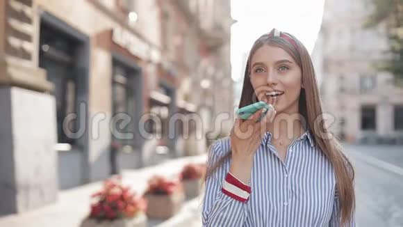 年轻漂亮的女士头戴棕色头发穿着时髦的条纹连衣裙用她的智能手机发声视频的预览图