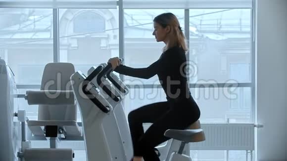 一个年轻的女人坐在健身房的运动自行车上背景是大镜子视频的预览图