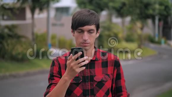 在城市郊区穿着红色格子衬衫的英俊白种人在手机上交谈的肖像背景是视频的预览图