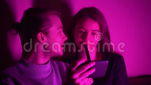 一个男人和他的女朋友坐在房间里看着他们的手机上的视频视频的预览图
