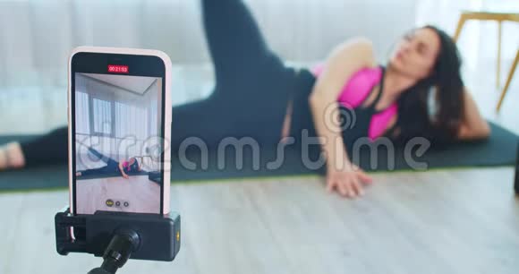 女人躺在瑜伽垫上伸展身体用电话录音4K视频的预览图