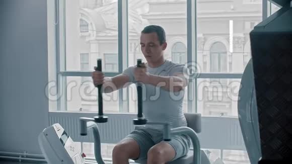 现代健身房一个穿白色t恤的年轻人在健身房锻炼手臂视频的预览图