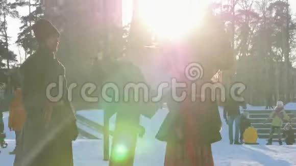 俄罗斯民间穿着民俗服装的女人在阳光明媚的天气里骑着秋千在冬天的公园里视频的预览图