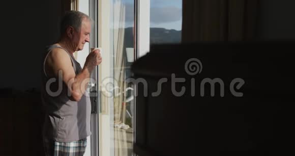 在窗户附近喝咖啡的老人视频的预览图