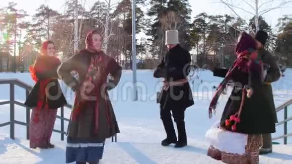 俄罗斯民间穿着鲜艳围巾的女人和男人在冬季公园的楼梯上跳舞视频的预览图
