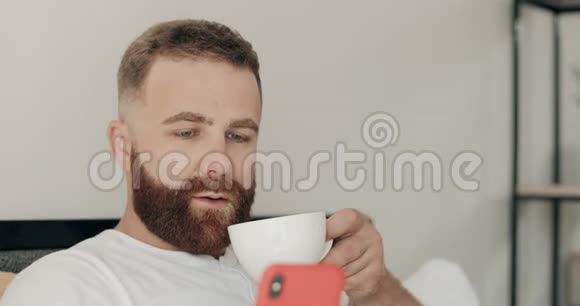 一群留胡子的年轻人用他的智能手机在早上喝咖啡时微笑着帅哥看起来视频的预览图