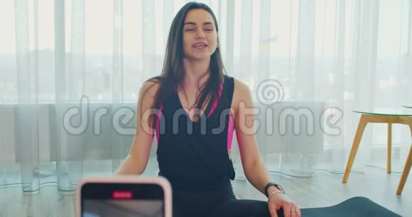 女人正在录制一段视频坐在瑜伽垫上聊天写体育博客视频的预览图