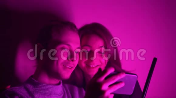 一个男人和他的女朋友坐在房间里看着他们的手机上的视频视频的预览图