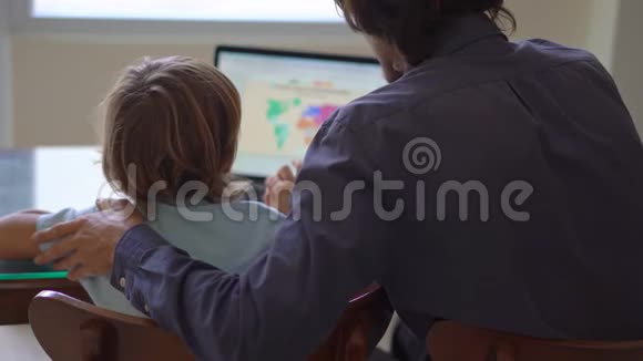 一个年轻人和他的小儿子在隔离期间坐在家里并在互联网学校使用平板电脑学习科罗纳视频的预览图