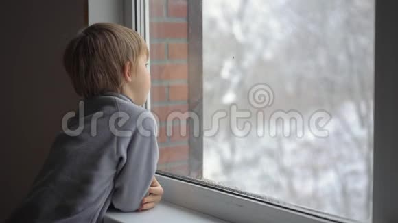 一个小男孩透过窗户看着一场大雪等待圣诞节的到来慢镜头视频的预览图