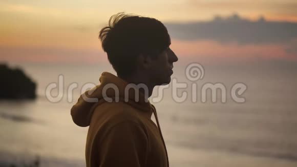 年轻人的肖像站在悬崖上看着大海男性感到幸福和安心日落视频的预览图