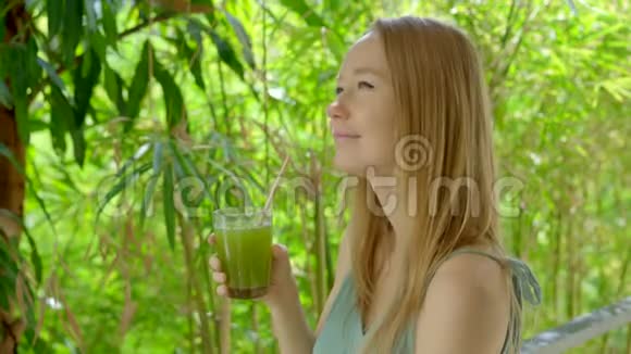 一个绿色环境中的年轻女子喝新鲜的芹菜汁视频的预览图
